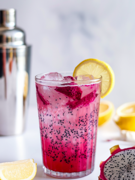 A vibrant pink Dragon Fruit Vodka Lemonade served over ice in a clear glass, garnished with a lemon slice and a wedge of fresh dragon fruit.