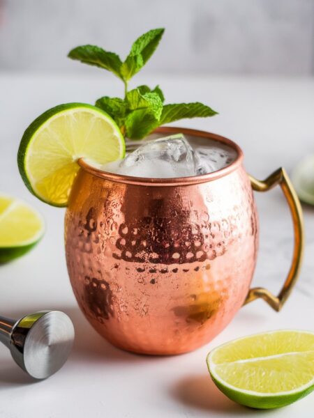 A refreshing Ginger Beer Mule Mocktail served in a glass with ice, fresh lime wedges, and mint sprigs, with bubbles rising to the surface.