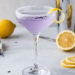 A beautifully crafted Lavender Lemon Drop Martini in a chilled glass, rimmed with sugar and garnished with a lemon twist and edible lavender flowers.