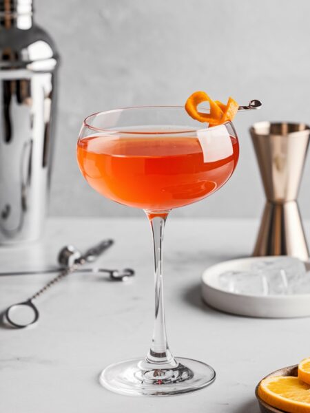 A vibrant orange Aperol Gin Martini served in a chilled martini glass with a delicate orange peel garnish, resting on a sleek cocktail napkin.