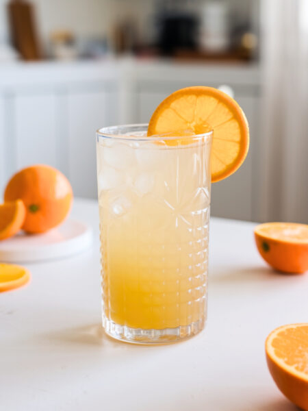 A refreshing glass of Classic Adrenal Mocktail with ice, garnished with an orange slice. The drink has a golden hue with a smooth, light texture.