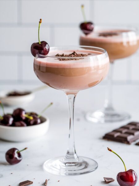 A Cherry Almond Kiss Mocktini in a chilled martini glass, garnished with a fresh cherry and chocolate shavings. The drink has a soft pink hue and smooth texture.