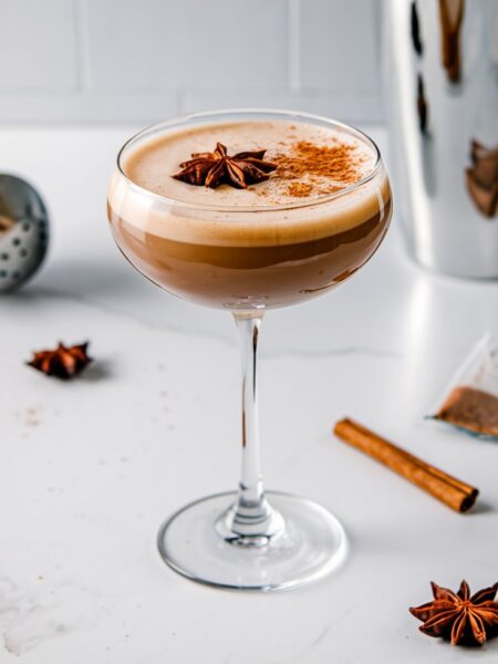 A creamy Chai Espresso Martini served in a sleek martini glass, topped with a sprinkle of cinnamon and garnished with a star anise. The drink has a rich, warm color and spiced aroma, perfect for cozy fall and winter gatherings.