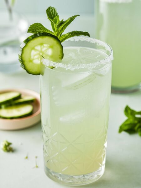 A refreshing Cucumber Elderflower Gin Fizz served in a tall glass with a cucumber wheel on the rim and a mint sprig garnish, perfect for summer.