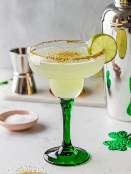 A golden margarita with a shimmering finish, served in a salt-rimmed glass with a lime wedge garnish.