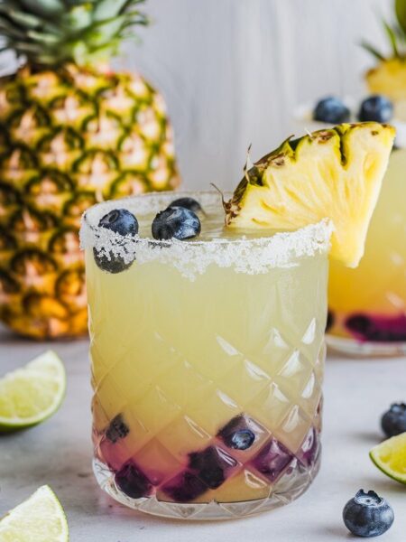 A vibrant Pineapple Blueberry Margarita served in a salt-rimmed glass, garnished with a pineapple wedge and fresh blueberries, perfect for summer.