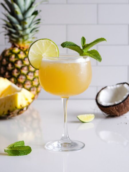 A tropical glass of Tropical Stress-Relief Drink with a golden hue, served over ice in a tall glass. The drink is garnished with a lime wedge and fresh mint, with condensation on the glass for a refreshing feel.