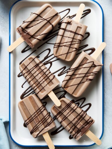 Creamy Espresso Martini Popsicles served on a tray, drizzled with chocolate and garnished with crushed espresso beans. The popsicles have a rich coffee color with a smooth, icy texture, perfect for summer parties.