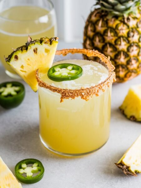 A vibrant Pineapple Jalapeño Margarita served in a glass with a Tajín rim, garnished with a pineapple wedge and jalapeño slice—perfect for summer.