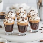 Espresso Martini Shots served in sleek shot glasses, topped with whipped cream and garnished with chocolate shavings. The drinks have a rich, dark base with a creamy, frothy topping, set against a bright, minimal background.