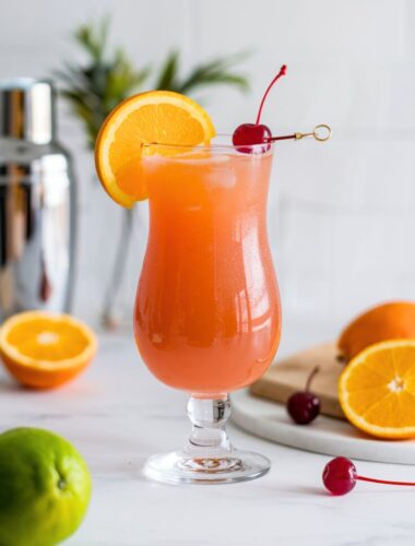 A vibrant Bahama Mama cocktail served in a hurricane glass, garnished with an orange slice and cherry, set against a tropical beach-inspired background.