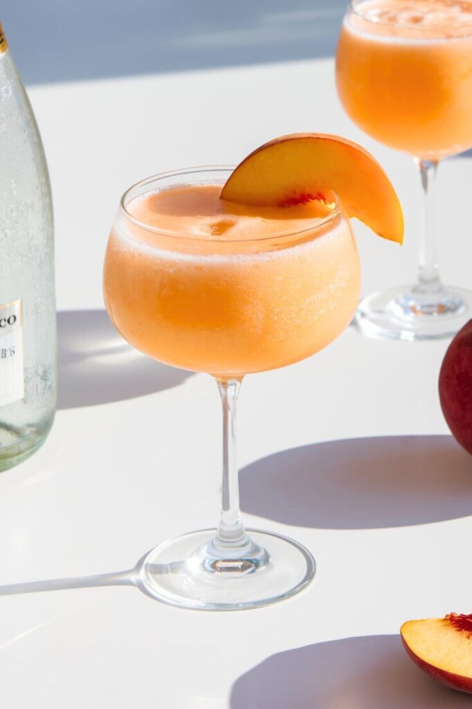 Refreshing frozen peach bellini cocktail with fresh peach slices