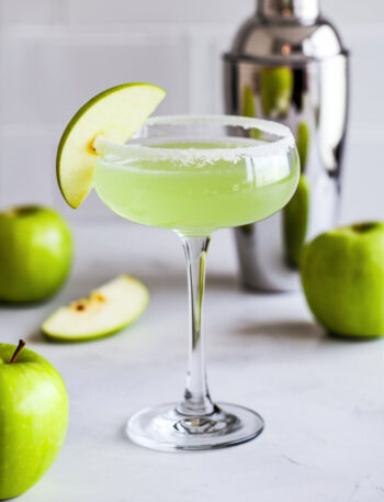 A vibrant Green Apple Glow Martini served in a chilled martini glass with a sugar rim, featuring a crisp green hue and garnished with a thin slice of fresh green apple.